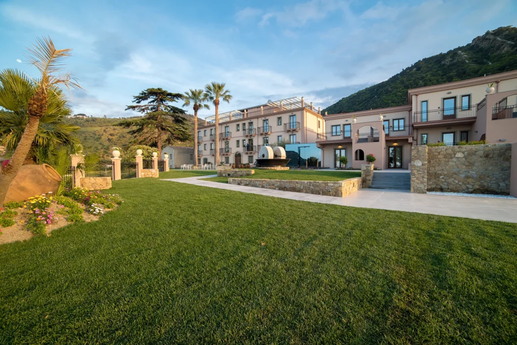 Esterno dell’hotel Terre di Eolo con giardini curati, vialetti pavimentati e vista sulle colline e sul mare.