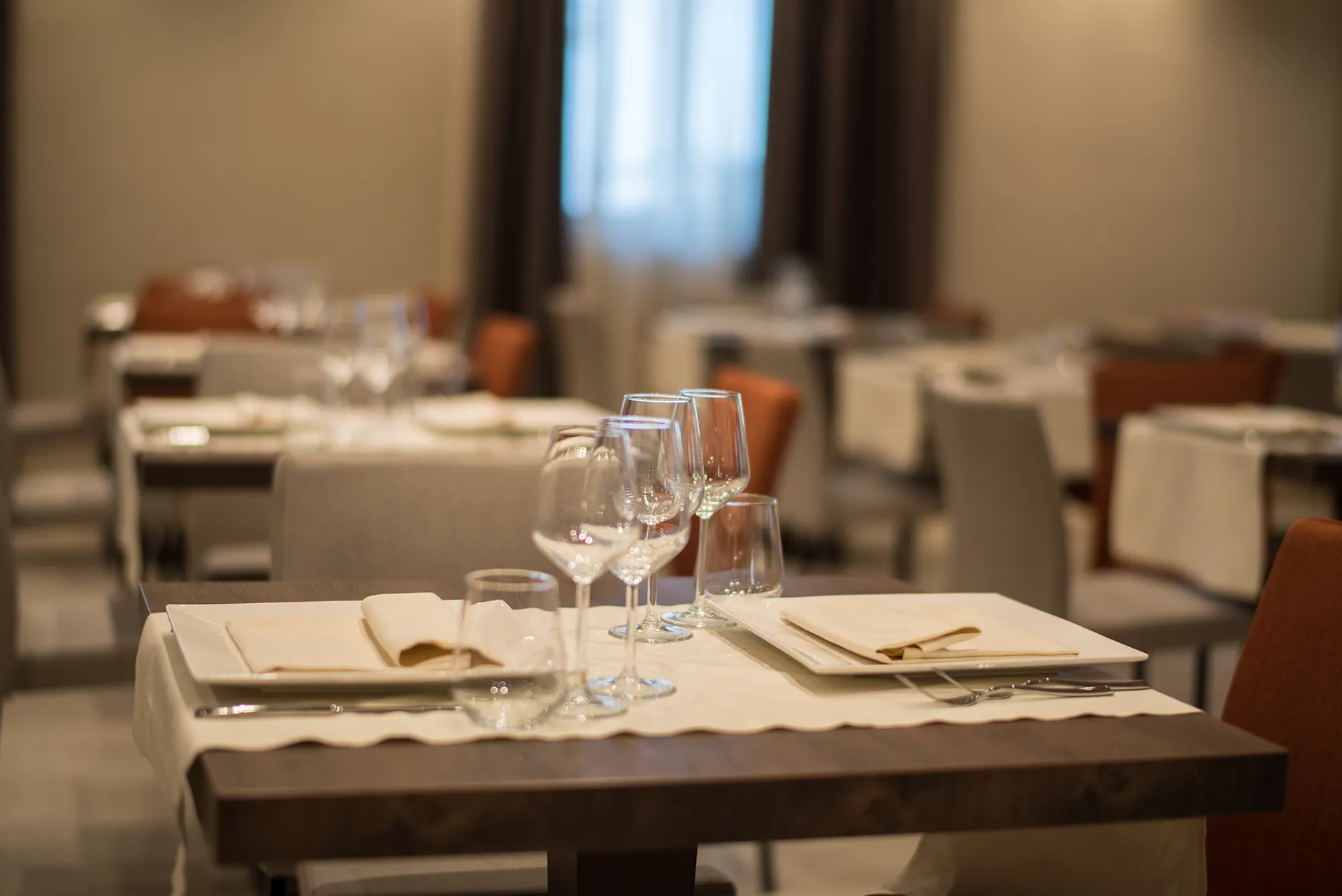 Sala interna del ristorante con tavoli apparecchiati, sedute moderne e illuminazione calda in ambiente elegante