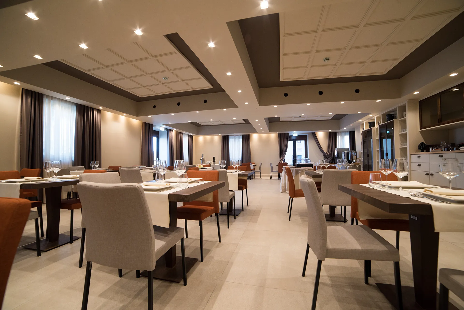 Sala interna del ristorante con tavoli apparecchiati, sedute moderne e illuminazione calda in ambiente elegante
