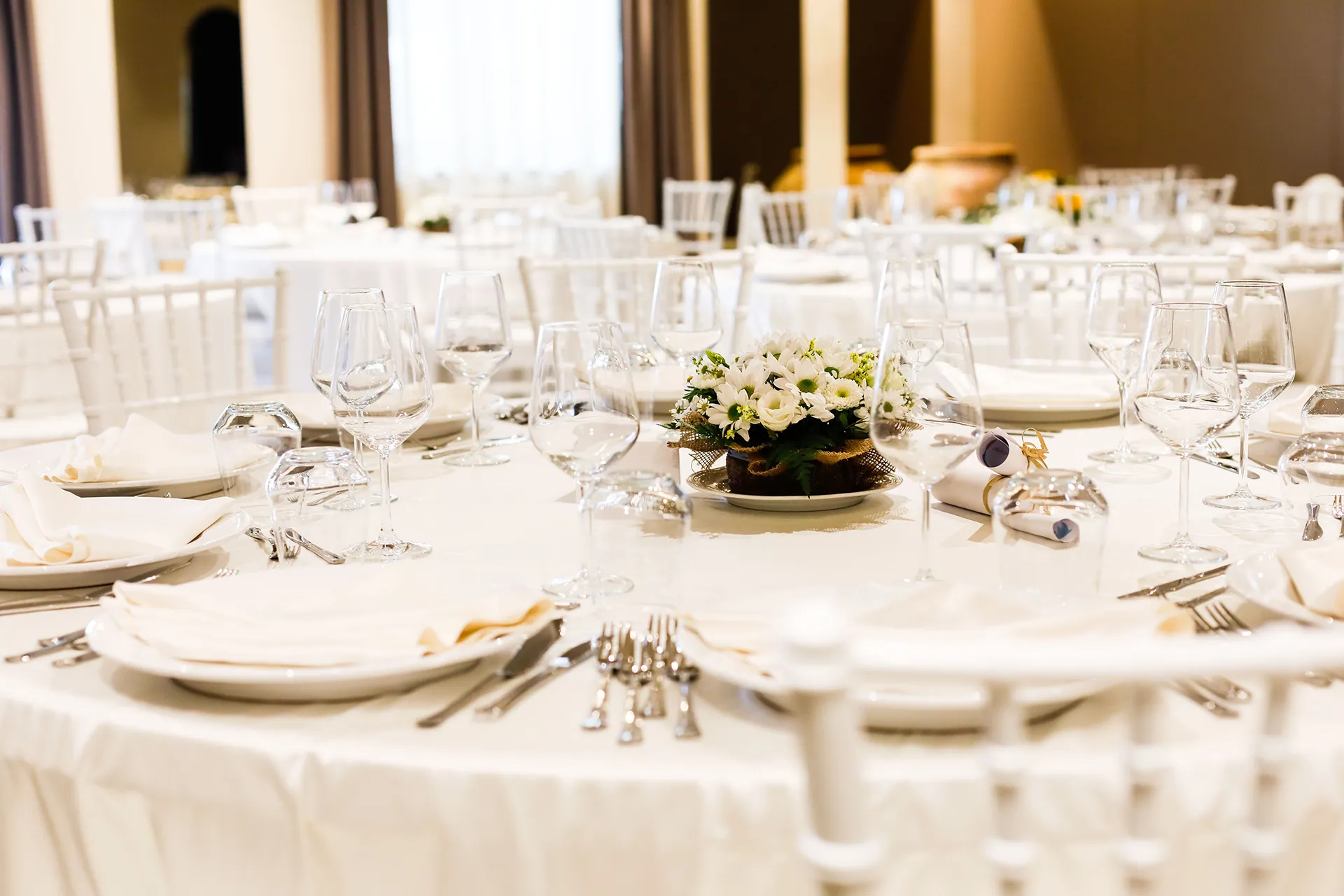 Tavolo elegantemente apparecchiato per evento all’interno dell’Hotel Terre di Eolo a Patti, con tovaglia bianca, calici di vetro, servizio di piatti e centrotavola floreale raffinato