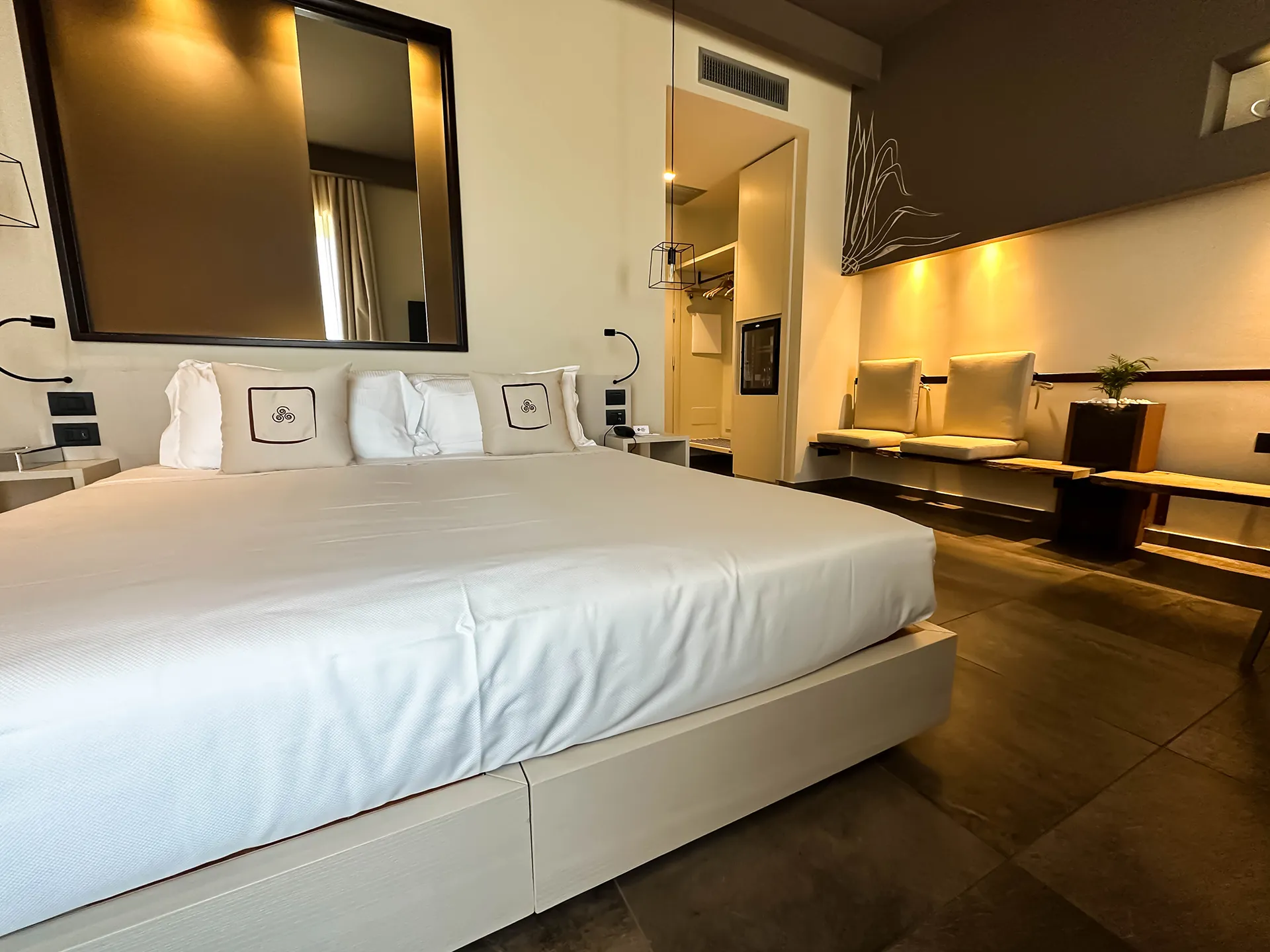 Camera moderna con due letti singoli affiancati, panca con cuscini, scrivania e illuminazione soft