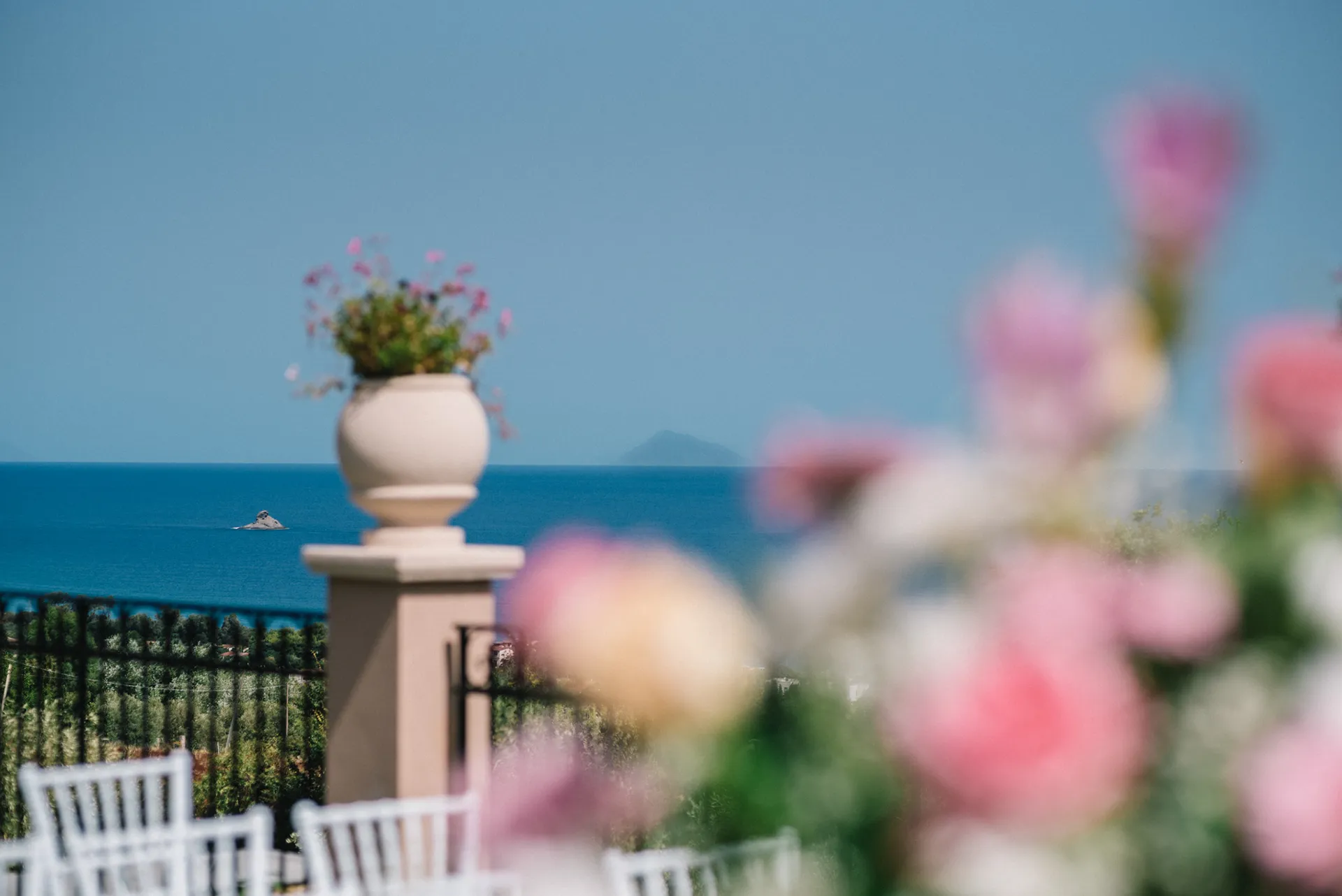 Terrazza panoramica dell’Hotel Terre di Eolo a Patti con vaso decorativo e vista sul mare, con fiori in primo piano sfocati che incorniciano il paesaggio.