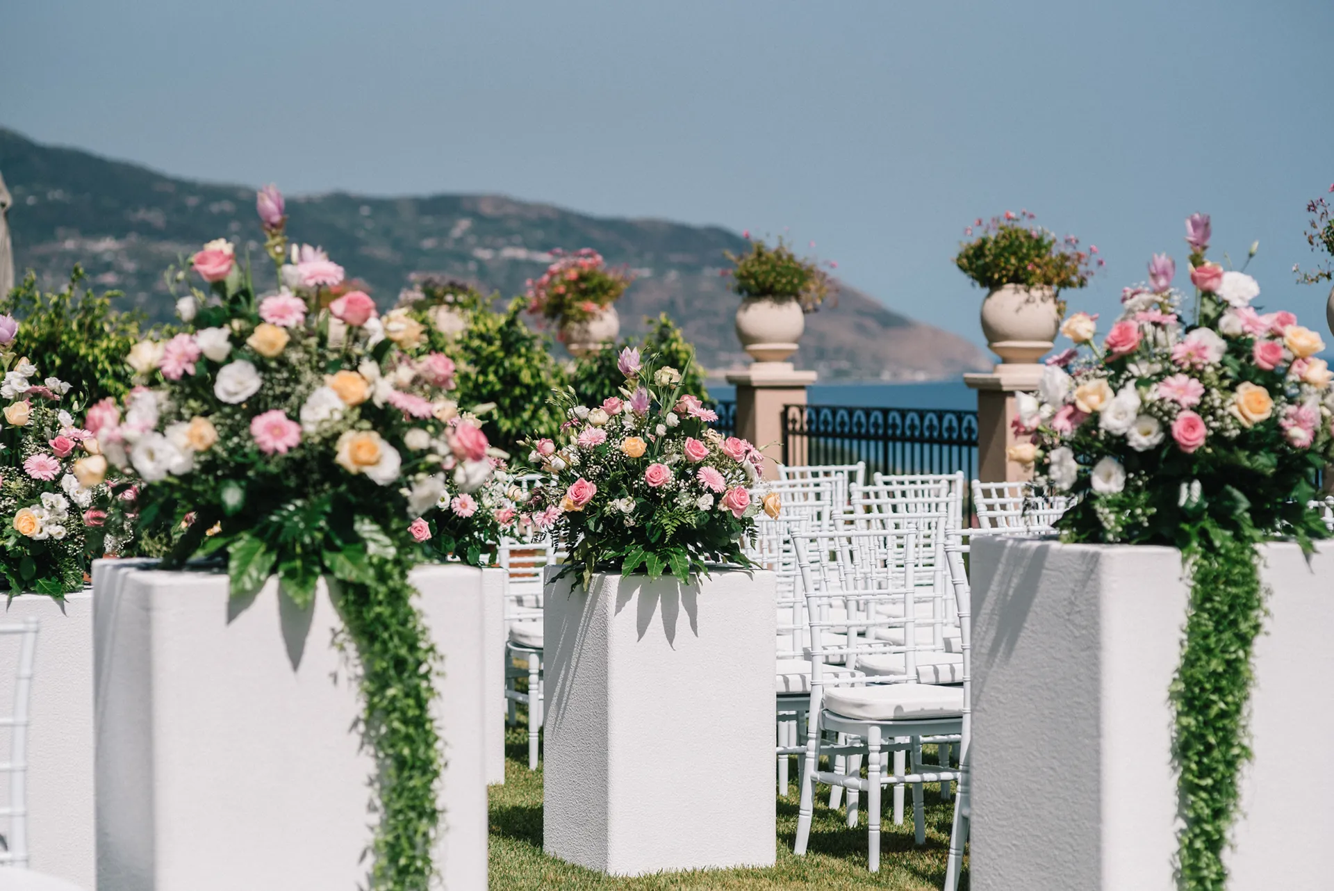 Giardino panoramico dell’Hotel Terre di Eolo a Patti allestito per una cerimonia all’aperto, con sedie bianche, composizioni floreali su piedistalli e vista sulle colline e sul mare.